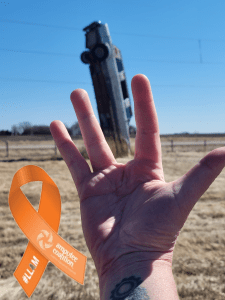 An old limousine sicking vertically out of a field as a sign post with my hand posed in front to make it appear as if the limo is replacing my amputated finger.